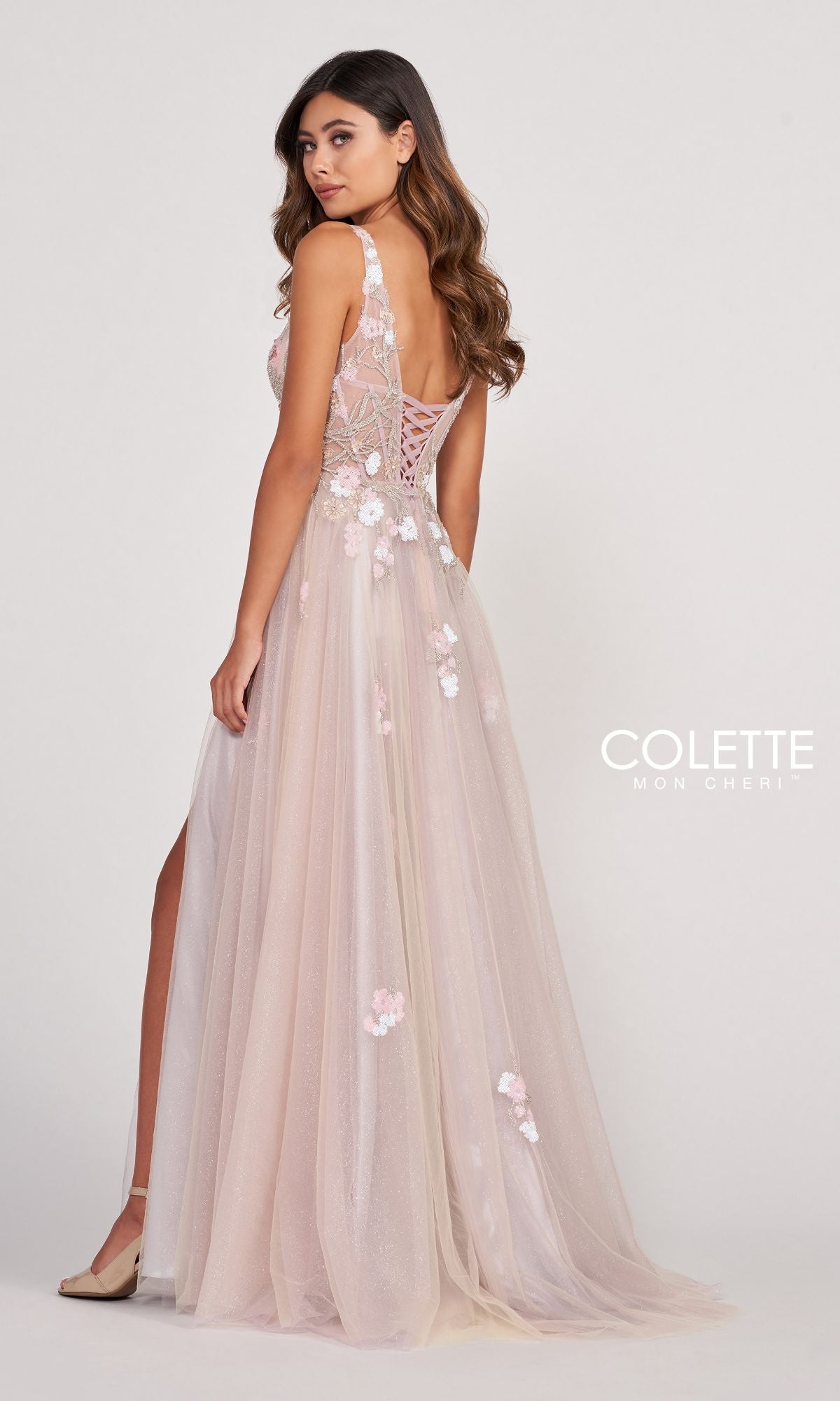 A woman in the Colette Corset-Back Silver Tulle Long Prom Dress stands sideways against a plain background, showcasing a graceful look with its floor-length tulle design and elegant corset back.